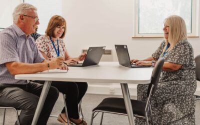 Three Invicta Law colleagues smiling and talking while working on laptops around conference table.