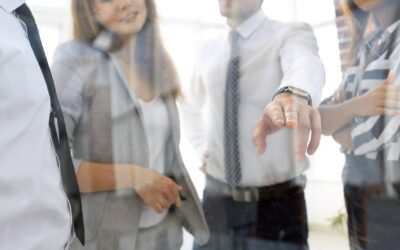 Four people in an office setting standing behind a window, one is pointing.