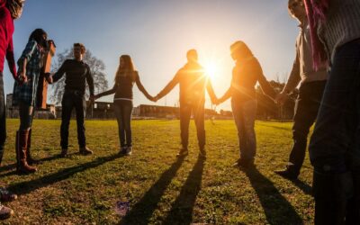 Group of young people standing in semi-circle bathed in golden sunlight, holding hands.