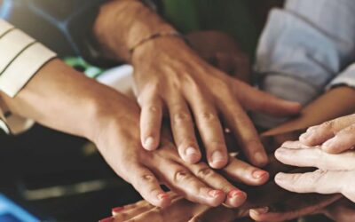 Circle of people with hands stacked in centre to depict community.