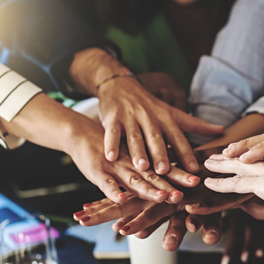 Circle of people with hands stacked in centre to depict community.